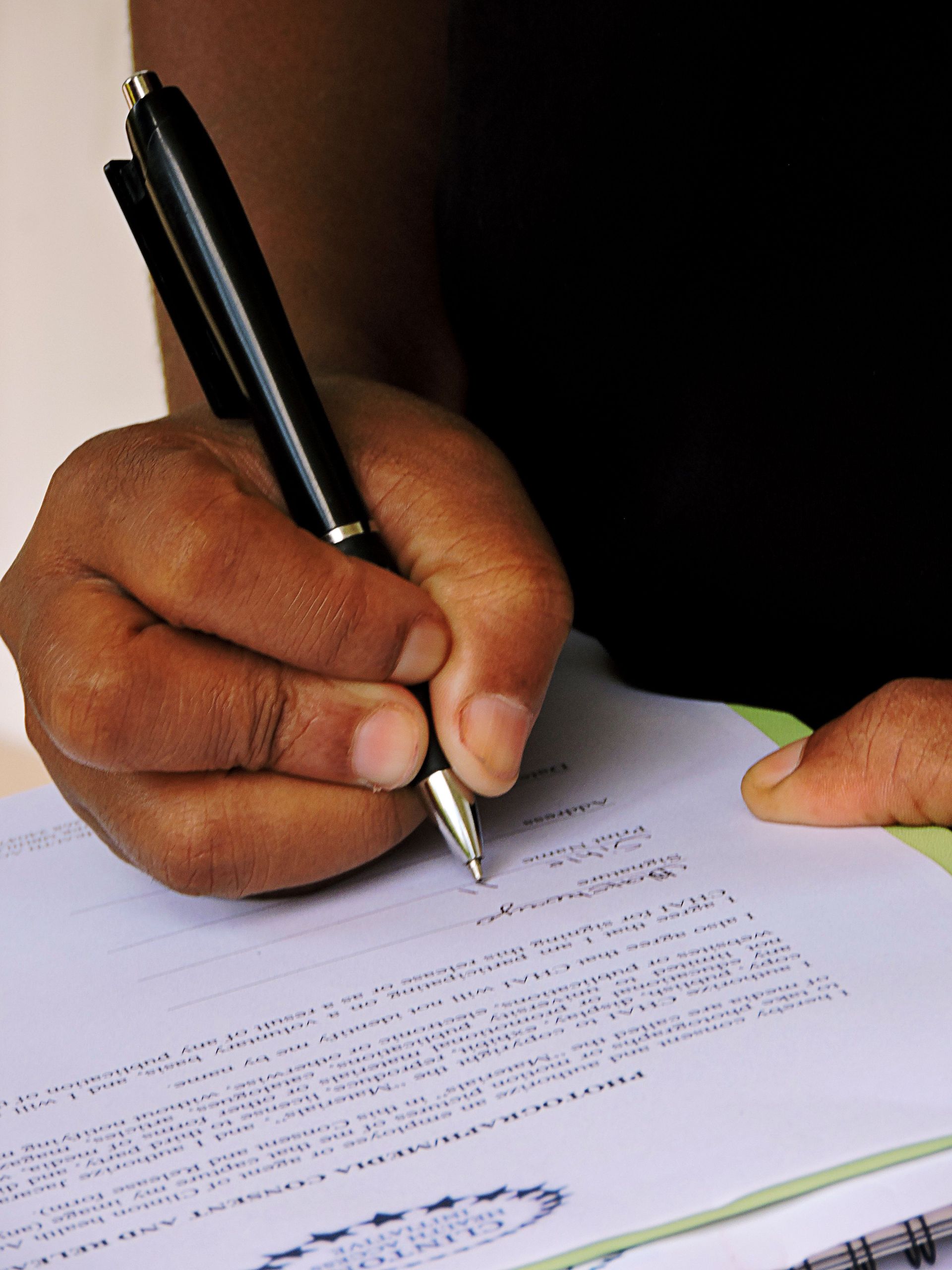 Person signing a document with a pen, emphasizing professionalism and formality.